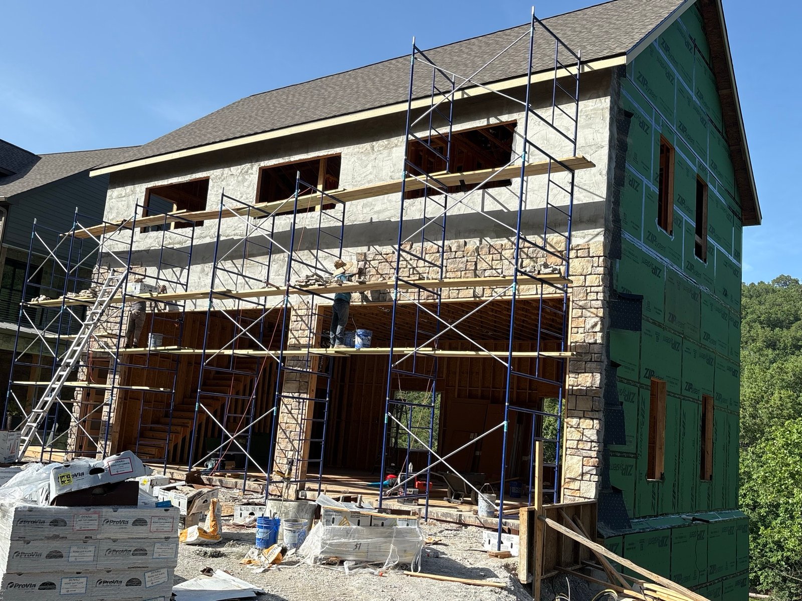Masons installing stone veneer on a two-story wall with scaffolding