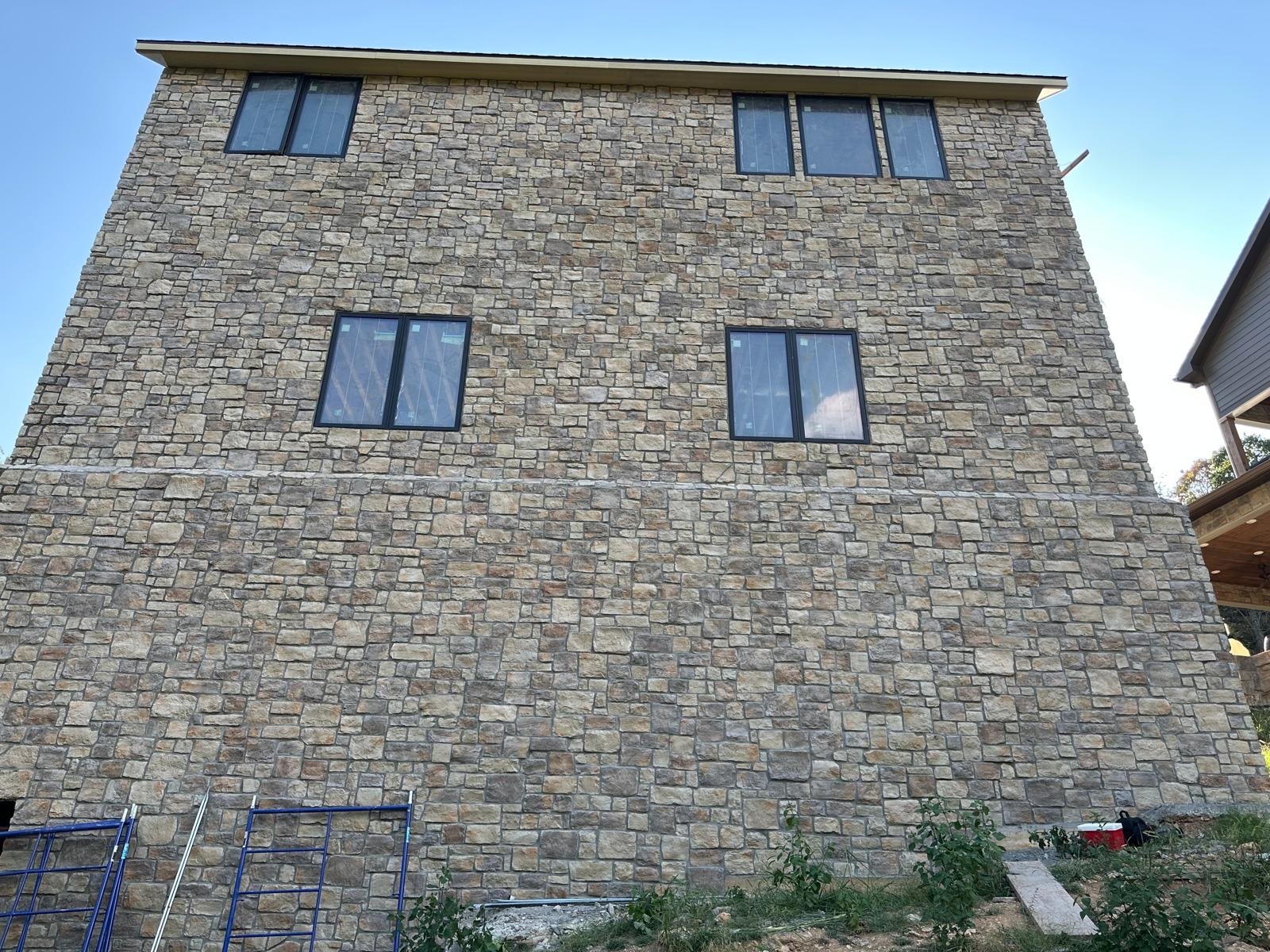 Finished three-story exterior wall in stacked stone veneer with dark-framed windows